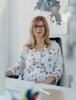 Inhaberin Britta Raab sitzt an ihrem Schreibtisch und schaut lächelnd in die Kamera
