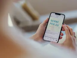 Detailaufnahme von zwei Händen, die ein Handy halten, auf dem Bildschirm steht Gerne per Du