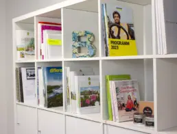 Weißes Bücherregal mit verschiedenen Broschüren, Magazinen und Büchern