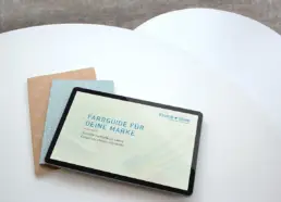 Zwei runde weiße Tisch von oben, darauf liegen gefächert zwei Notizbücher und ein Tablet mit der Farbguide-Ansicht