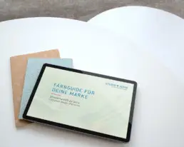 Zwei runde weiße Tisch von oben, darauf liegen gefächert zwei Notizbücher und ein Tablet mit der Farbguide-Ansicht