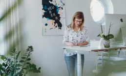 Inhaberin Britta Raab steht lächelnd am Steh-Schreibtisch und blickt in ein Notizbuch